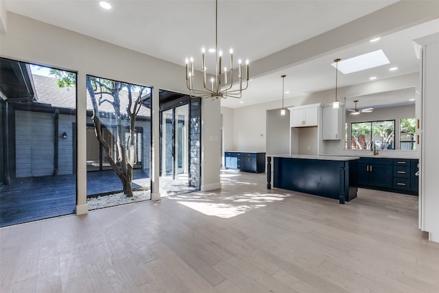 kitchen featuring a skylight, a kitchen island, white cabinetry, pendant lighting, and light hardwood / wood-style flooring