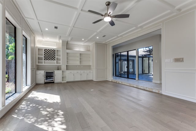 unfurnished living room with beverage cooler, ceiling fan, light hardwood / wood-style flooring, built in shelves, and coffered ceiling