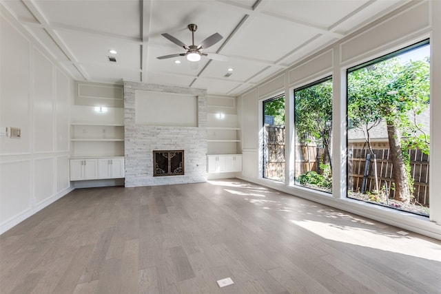 unfurnished living room featuring coffered ceiling, built in features, ceiling fan, a fireplace, and light hardwood / wood-style floors