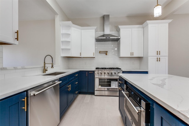 kitchen featuring decorative light fixtures, appliances with stainless steel finishes, wall chimney exhaust hood, and blue cabinets