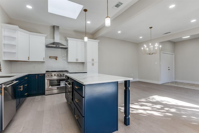 kitchen with white cabinetry, blue cabinetry, wall chimney exhaust hood, and stainless steel appliances