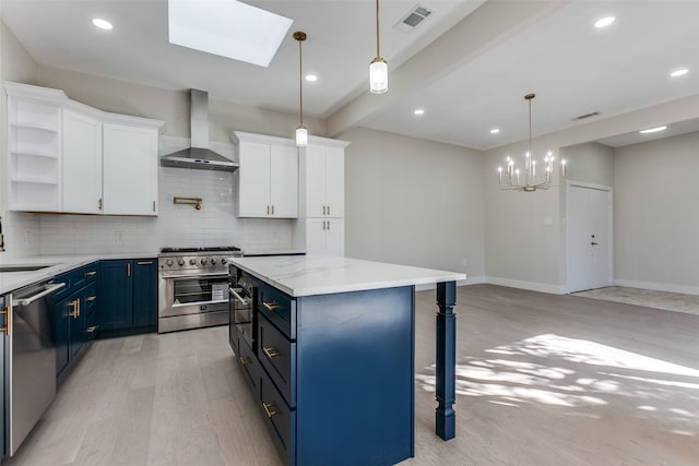 kitchen with appliances with stainless steel finishes, white cabinetry, blue cabinetry, light hardwood / wood-style flooring, and wall chimney exhaust hood