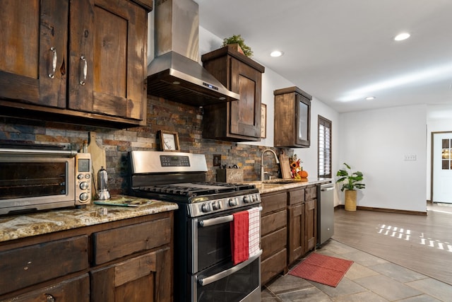 kitchen featuring wall chimney exhaust hood, light stone countertops, appliances with stainless steel finishes, and sink