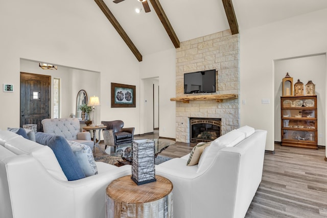 living room with ceiling fan, wood-type flooring, beam ceiling, a stone fireplace, and high vaulted ceiling