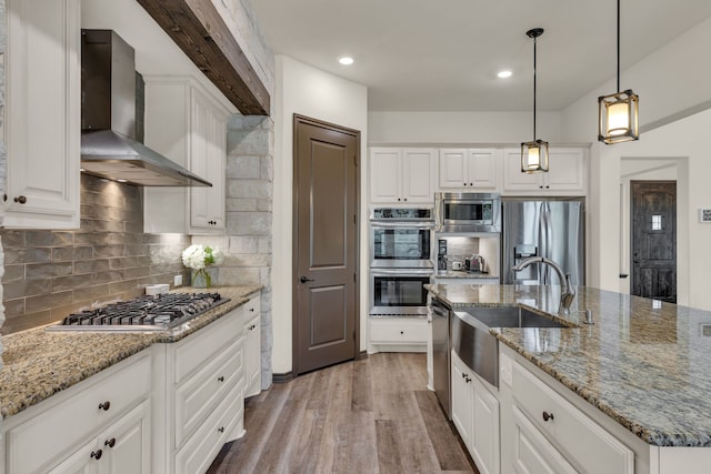 kitchen with wall chimney range hood, light hardwood / wood-style floors, pendant lighting, white cabinets, and appliances with stainless steel finishes