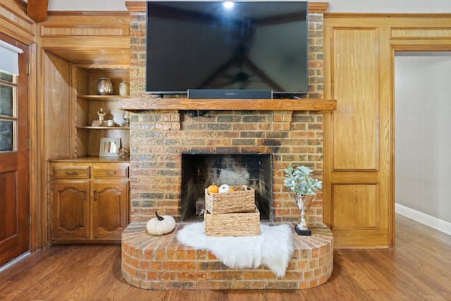 interior details featuring hardwood / wood-style flooring, wooden walls, built in shelves, and a brick fireplace