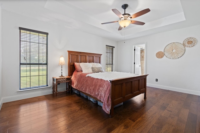 bedroom with a raised ceiling, connected bathroom, dark hardwood / wood-style flooring, and ceiling fan