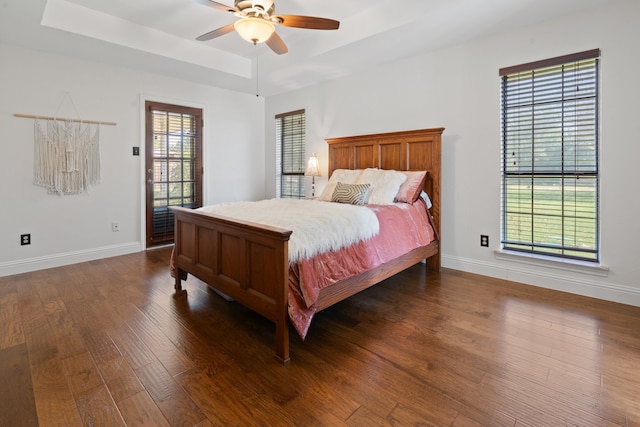 bedroom with ceiling fan, a tray ceiling, and dark wood-type flooring