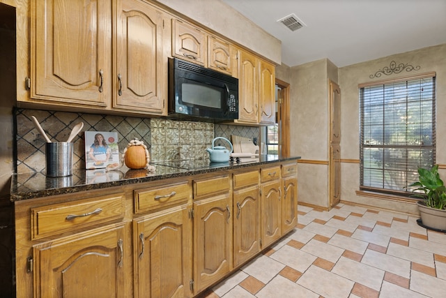 kitchen featuring dark stone countertops, black appliances, and backsplash