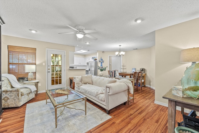 living room featuring ceiling fan with notable chandelier, a textured ceiling, and light hardwood / wood-style flooring