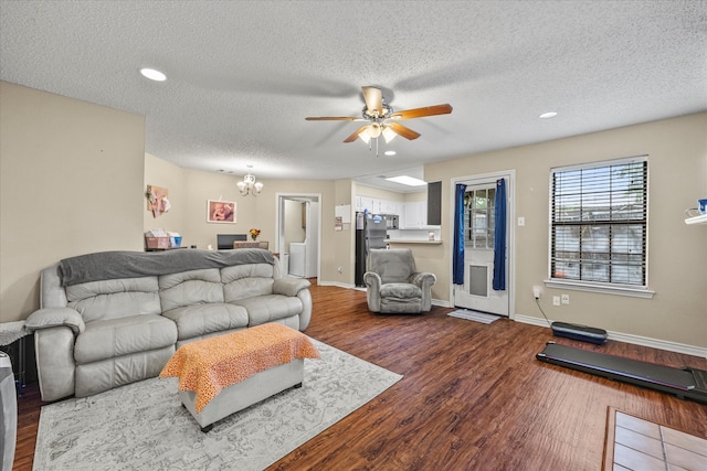 living room with ceiling fan with notable chandelier, dark hardwood / wood-style flooring, and a textured ceiling