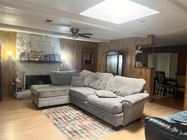 living room with a skylight, ceiling fan, a textured ceiling, wooden walls, and hardwood / wood-style flooring