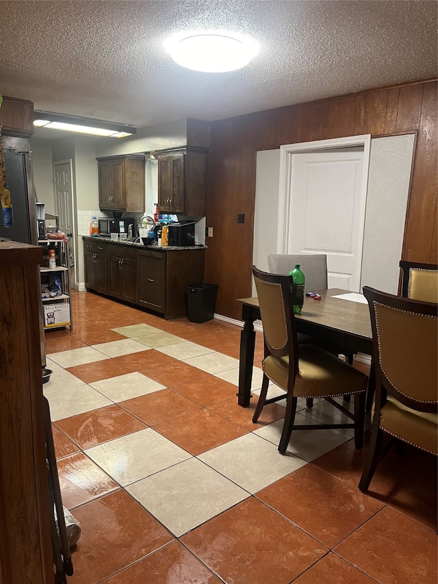 interior space with wooden walls, dark brown cabinetry, a textured ceiling, and light tile patterned floors