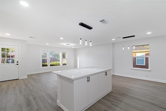 kitchen with light hardwood / wood-style flooring, a kitchen island, pendant lighting, light stone countertops, and white cabinets