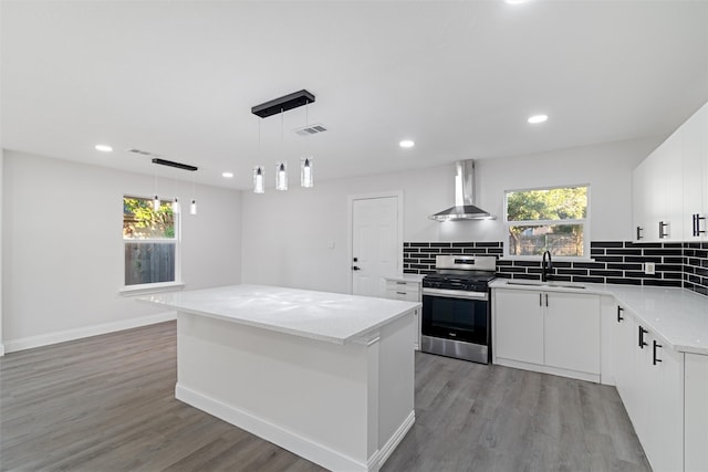 kitchen with white cabinets, a center island, wall chimney range hood, and stainless steel stove