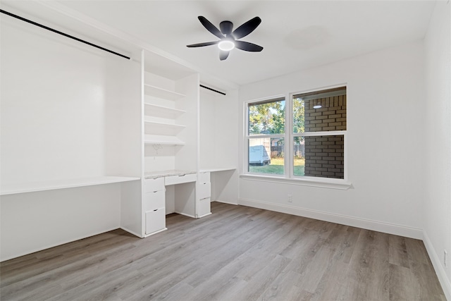 unfurnished bedroom with built in desk, ceiling fan, and light hardwood / wood-style flooring