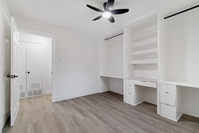 unfurnished bedroom with ceiling fan, built in desk, and light wood-type flooring