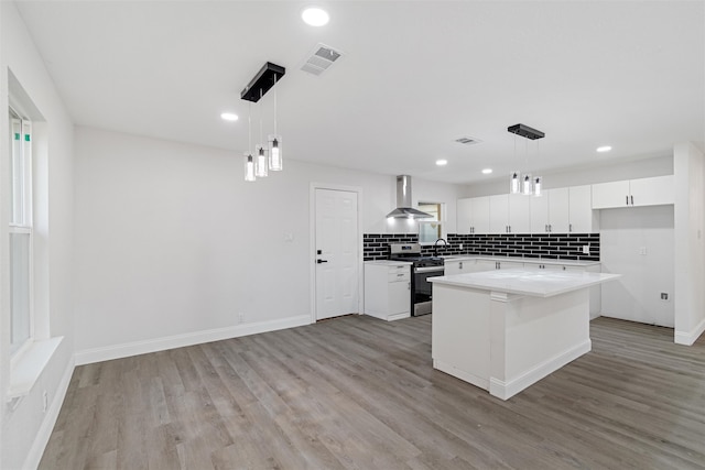 kitchen featuring wall chimney exhaust hood, decorative light fixtures, stainless steel stove, a kitchen island, and white cabinets