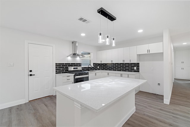 kitchen with white cabinetry, stainless steel gas range, ventilation hood, and a kitchen island