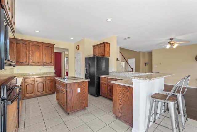 kitchen featuring a kitchen bar, light tile patterned floors, kitchen peninsula, a kitchen island, and black appliances