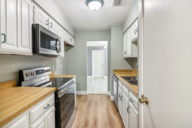 kitchen featuring sink, light hardwood / wood-style floors, white cabinetry, appliances with stainless steel finishes, and a textured ceiling