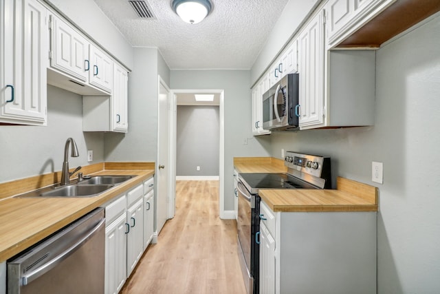 kitchen with sink, a textured ceiling, light hardwood / wood-style flooring, white cabinetry, and appliances with stainless steel finishes