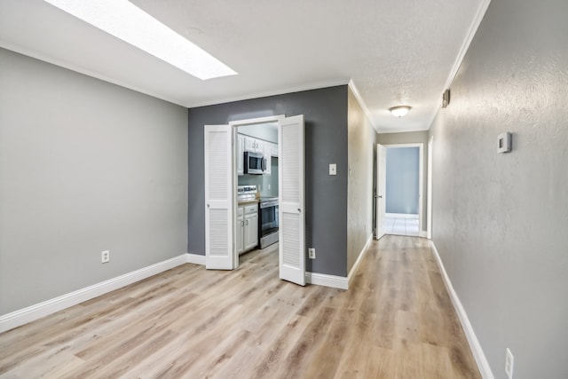 hall with a skylight, light wood-type flooring, and ornamental molding