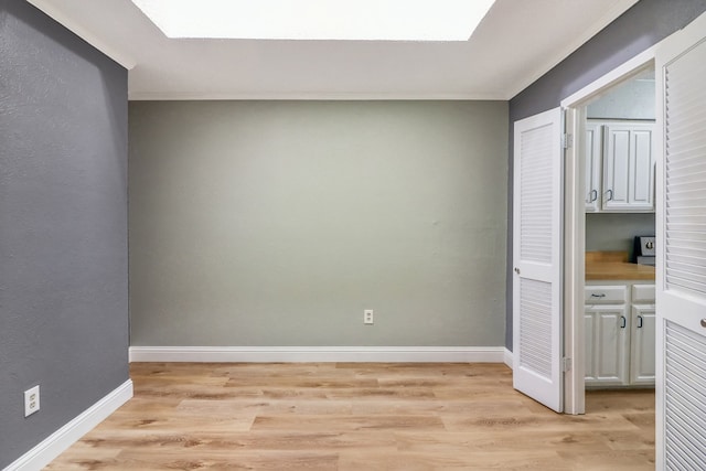 empty room featuring a skylight, crown molding, and light hardwood / wood-style floors