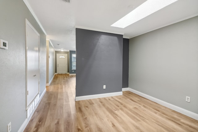 spare room featuring a skylight, crown molding, and light hardwood / wood-style floors