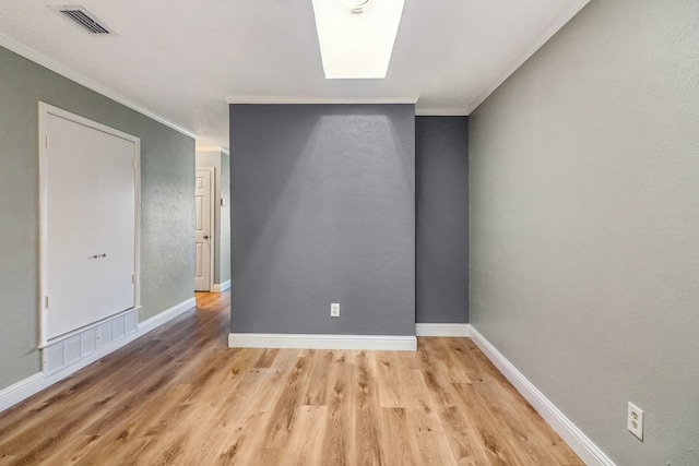 spare room featuring ornamental molding, a skylight, and light hardwood / wood-style flooring