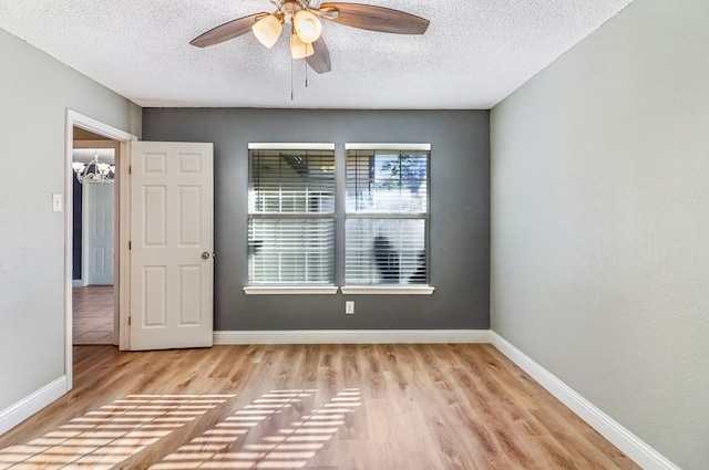 empty room featuring ceiling fan with notable chandelier, a textured ceiling, and light hardwood / wood-style flooring