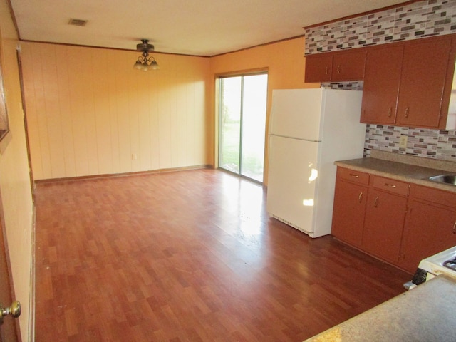 kitchen with ceiling fan, white refrigerator, wood walls, tasteful backsplash, and dark wood-type flooring