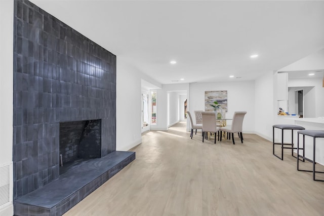 dining area featuring recessed lighting, light wood-type flooring, a tiled fireplace, and baseboards