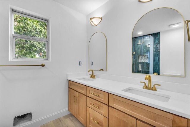 bathroom featuring double vanity, a shower stall, wood finished floors, and a sink