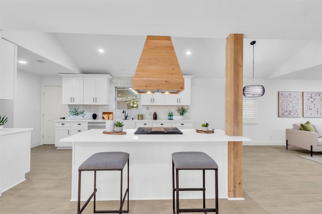 kitchen featuring cooktop, decorative backsplash, a breakfast bar area, light countertops, and lofted ceiling