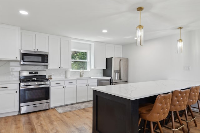 kitchen with white cabinetry, sink, stainless steel appliances, light hardwood / wood-style flooring, and decorative light fixtures