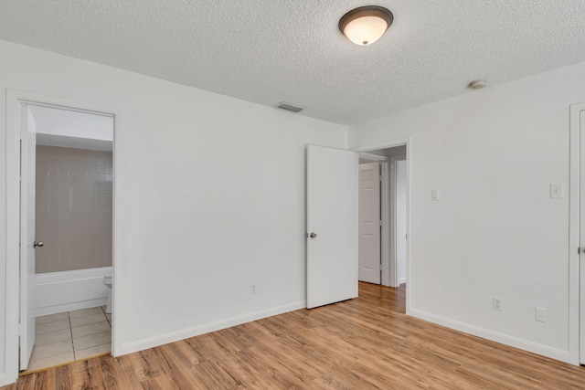 unfurnished bedroom with a textured ceiling, connected bathroom, and light wood-type flooring