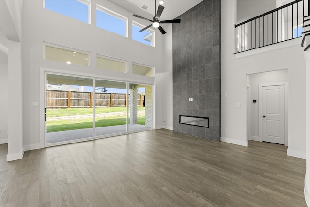 unfurnished living room with hardwood / wood-style floors, a tiled fireplace, a high ceiling, and ceiling fan