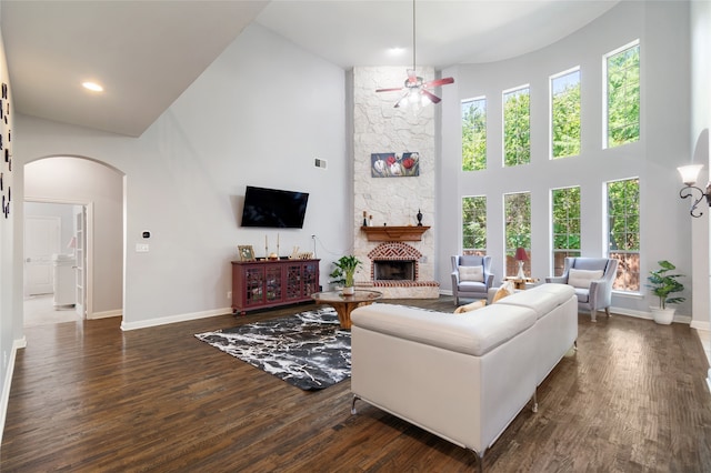 living room featuring ceiling fan, a stone fireplace, a towering ceiling, and dark hardwood / wood-style flooring