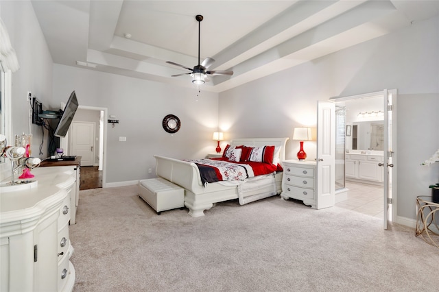 bedroom with light carpet, ensuite bath, a tray ceiling, and ceiling fan