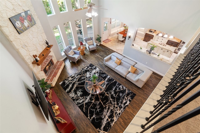 living room featuring a towering ceiling, dark wood-type flooring, a fireplace, and ceiling fan