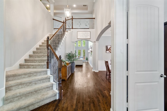 entrance foyer with an inviting chandelier, decorative columns, dark wood-type flooring, and a high ceiling