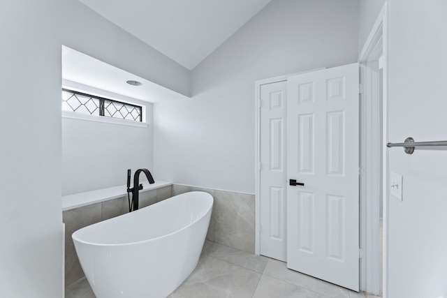 bathroom with tile walls, lofted ceiling, tile patterned floors, and a bathing tub