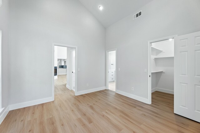 interior space featuring a closet, a walk in closet, ensuite bath, high vaulted ceiling, and light hardwood / wood-style floors