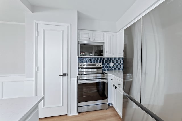 kitchen featuring light wood-type flooring, white cabinetry, stainless steel appliances, and backsplash