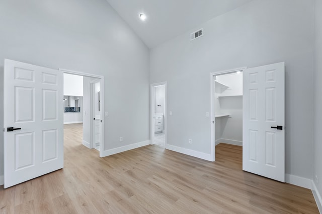 unfurnished bedroom with a spacious closet, high vaulted ceiling, light wood-type flooring, ensuite bathroom, and a closet