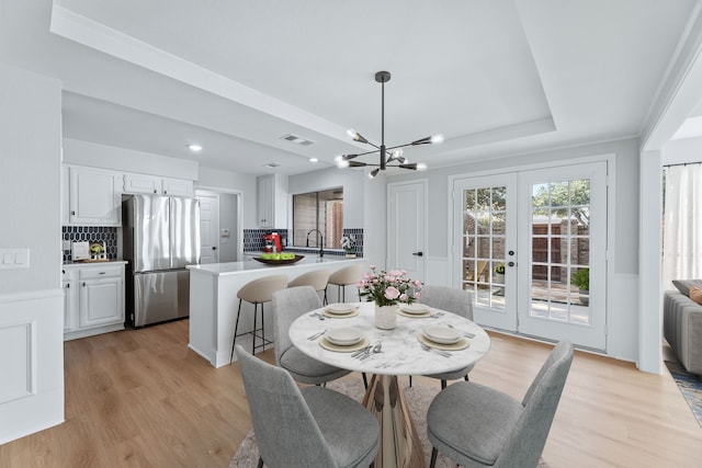 dining area featuring french doors, light hardwood / wood-style flooring, a tray ceiling, ornamental molding, and a chandelier