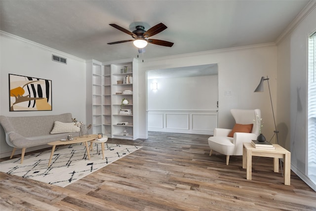 sitting room with built in shelves, ceiling fan, wood-type flooring, and ornamental molding