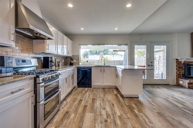 kitchen featuring wall chimney range hood, light hardwood / wood-style flooring, double oven range, black dishwasher, and white cabinetry