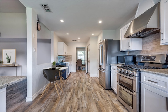 kitchen featuring wall chimney exhaust hood, stainless steel gas range oven, white cabinetry, and light hardwood / wood-style flooring